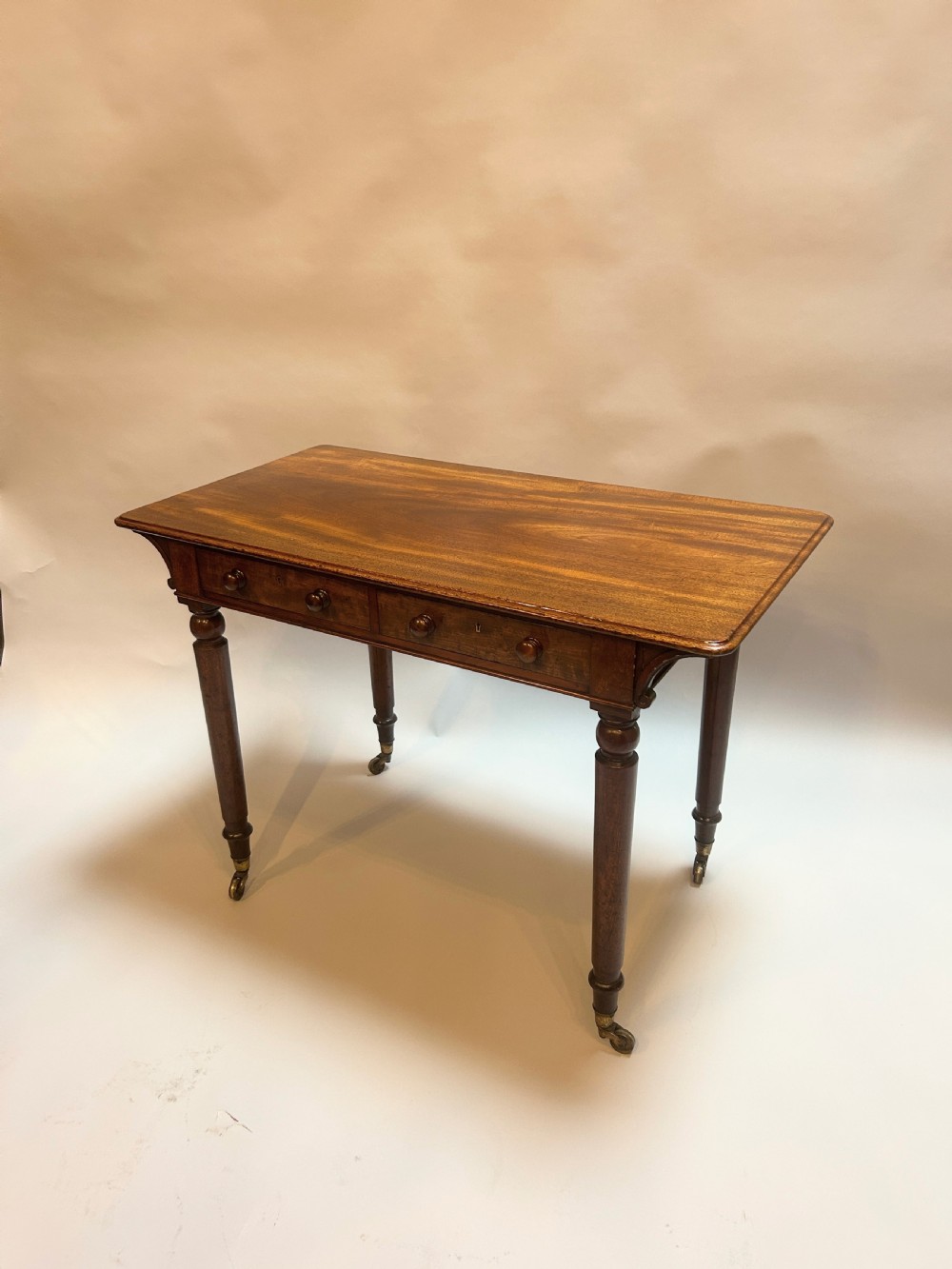A Victorian mahogany writing table featuring two frieze drawers with turned wooden knob handles and turned legs supported by brass castors.