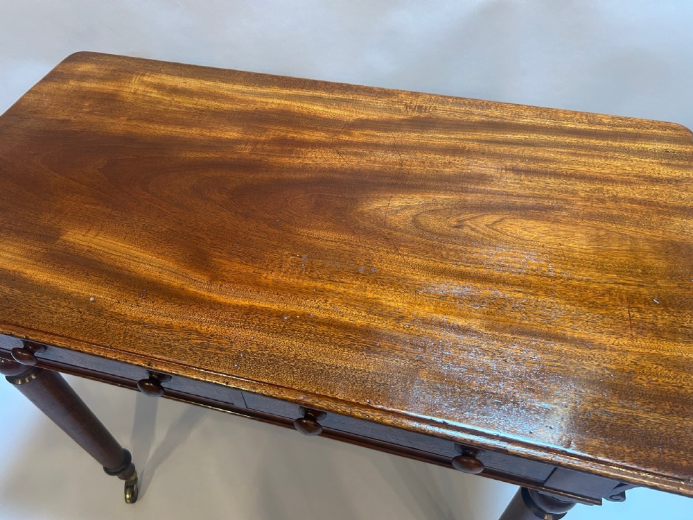 A Victorian mahogany writing table featuring two frieze drawers with turned wooden knob handles and turned legs supported by brass castors. View II