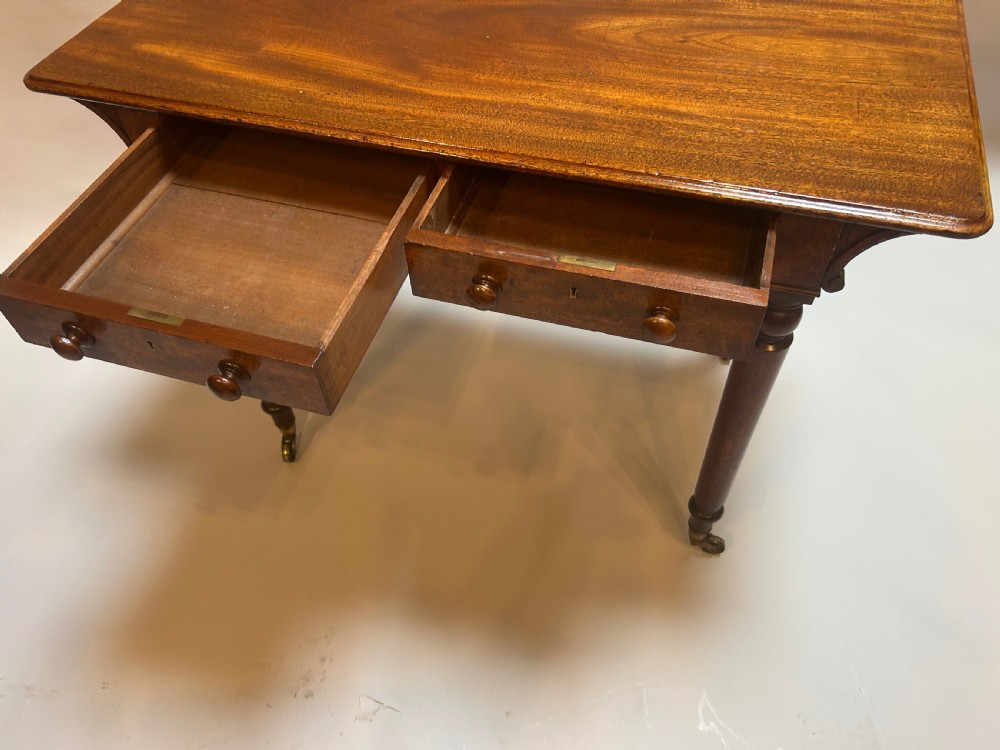 A Victorian mahogany writing table featuring two frieze drawers with turned wooden knob handles and turned legs supported by brass castors. View IV