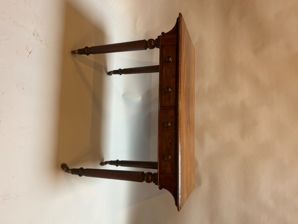 A Victorian mahogany writing table featuring two frieze drawers with turned wooden knob handles and turned legs supported by brass castors. View V