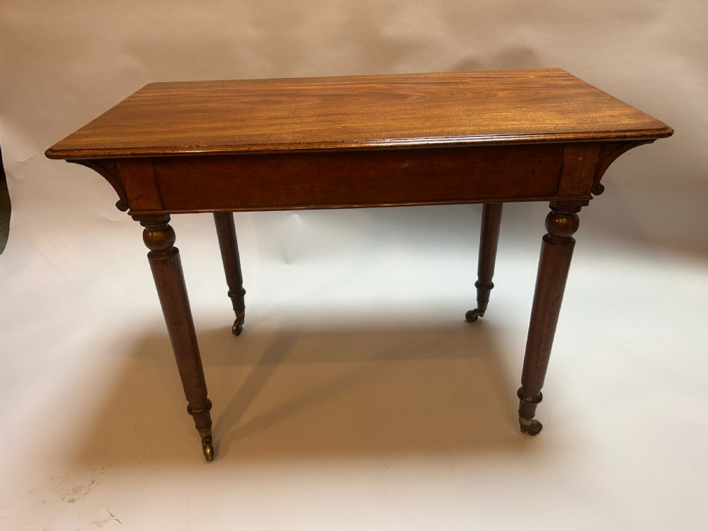 A Victorian mahogany writing table featuring two frieze drawers with turned wooden knob handles and turned legs supported by brass castors. View VIII
