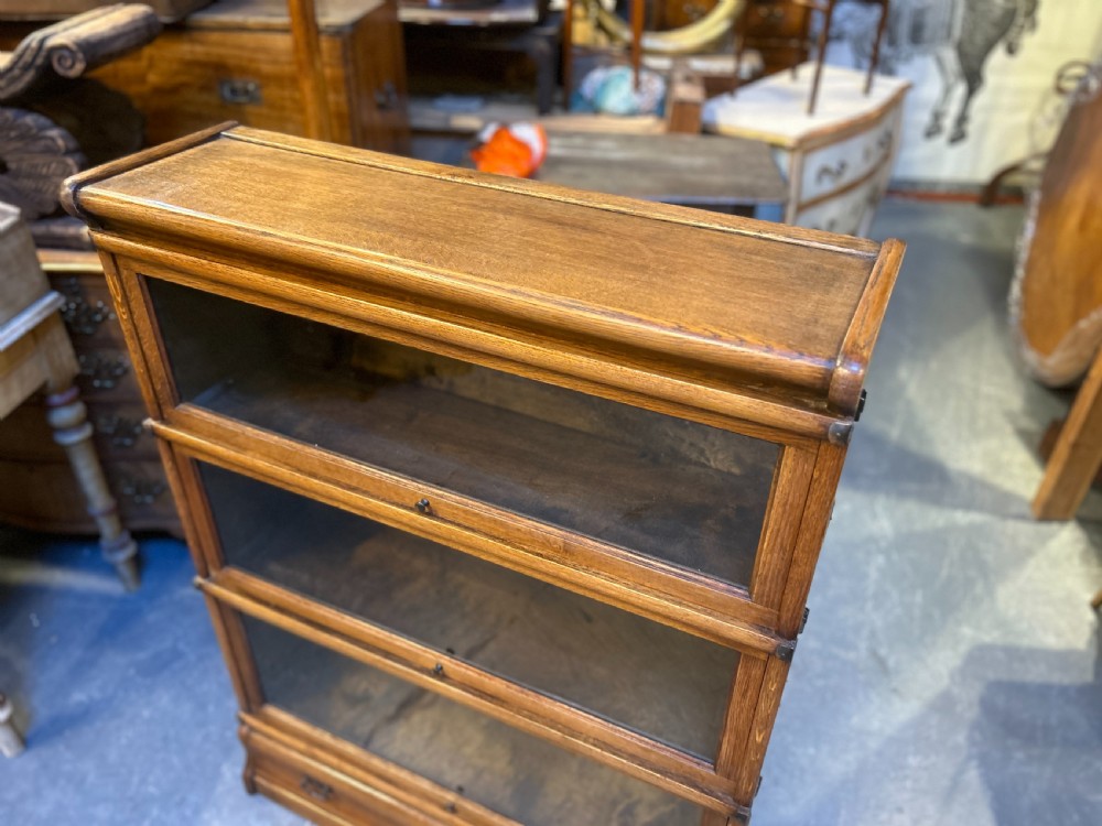 A three-tier antique oak Globe Wernicke stacking bookcase featuring glazed lift-up doors and a base drawer. View X