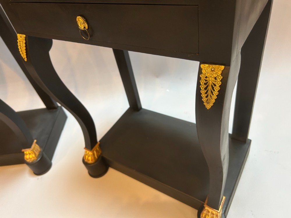 A pair of ebonised black French Empire style bedside chests featuring grey marble tops, three small drawers with ring pulls, curved front legs with gilt paw feet, and an undertier shelf. View III