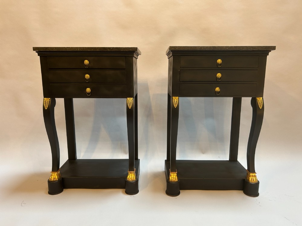 A pair of ebonised black French Empire style bedside chests featuring grey marble tops, three small drawers with ring pulls, curved front legs with gilt paw feet, and an undertier shelf. View VI