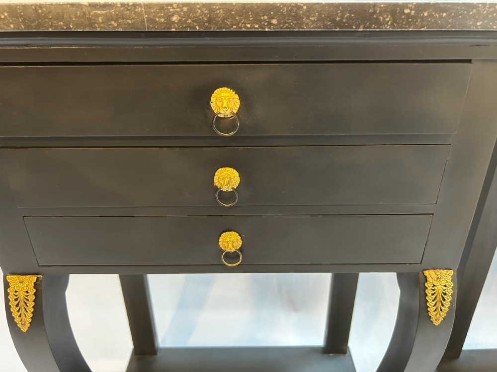 A pair of ebonised black French Empire style bedside chests featuring grey marble tops, three small drawers with ring pulls, curved front legs with gilt paw feet, and an undertier shelf. View VII