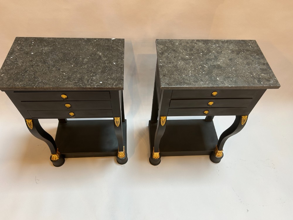 A pair of ebonised black French Empire style bedside chests featuring grey marble tops, three small drawers with ring pulls, curved front legs with gilt paw feet, and an undertier shelf. View VIII