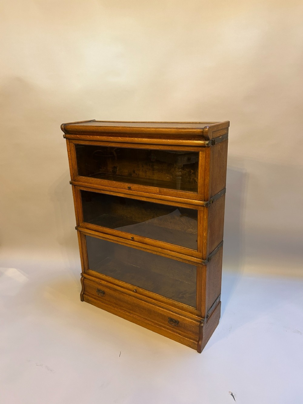 A three-tier antique oak Globe Wernicke stacking bookcase featuring glazed lift-up doors and a base drawer.