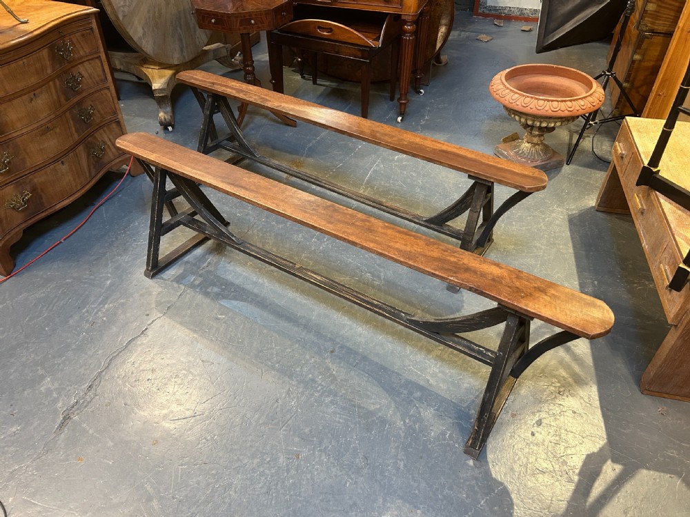 A pair of long wooden benches featuring warm brown timber plank tops supported by black painted trestle bases. View VI