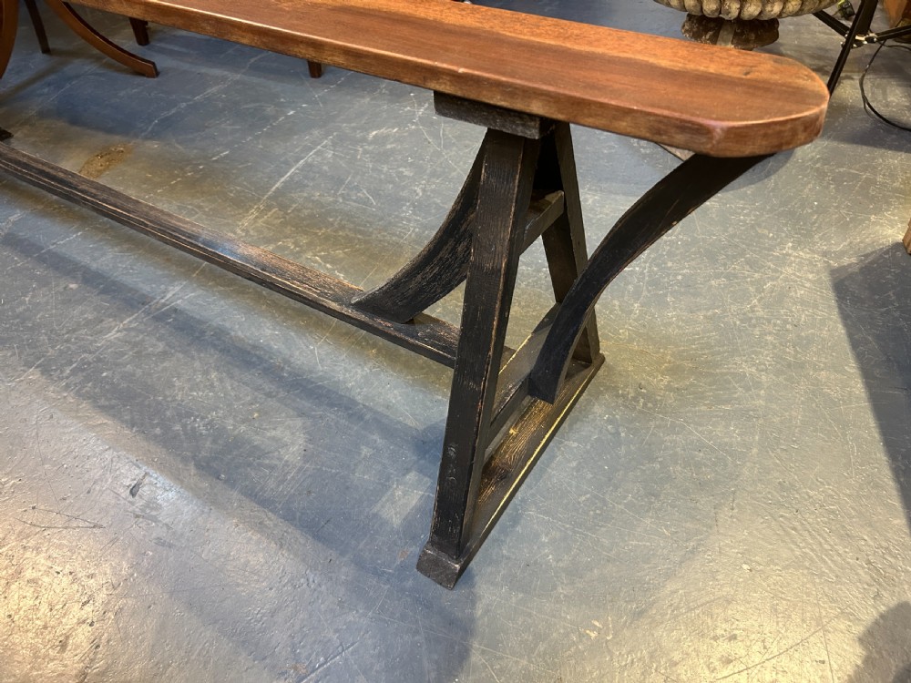 A pair of long wooden benches featuring warm brown timber plank tops supported by black painted trestle bases. View VII