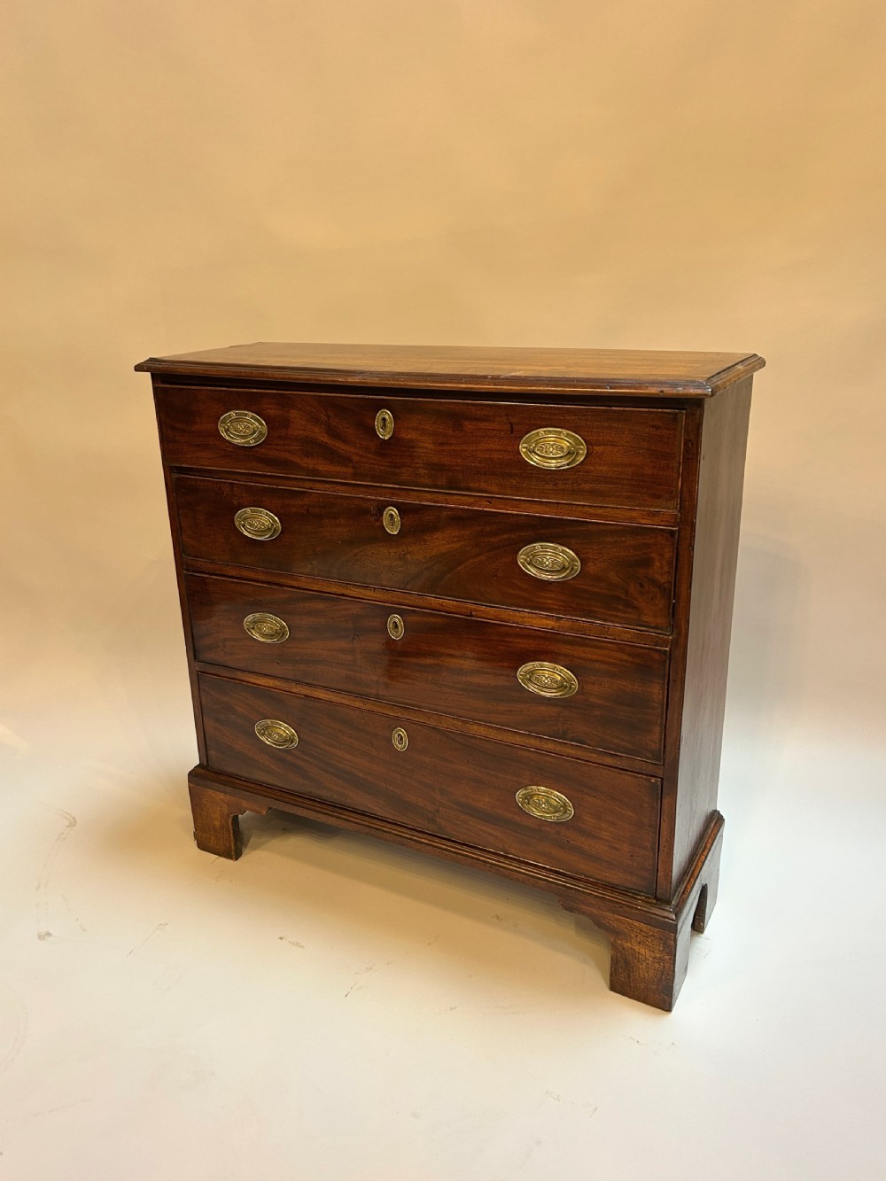 A George III dark mahogany hall chest of drawers with four graduated drawers, oval brass handles, and bracket feet.