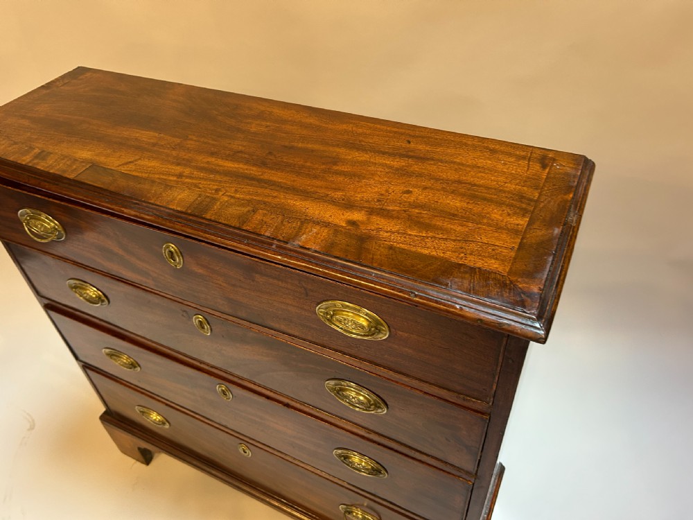A George III dark mahogany hall chest of drawers with four graduated drawers, oval brass handles, and bracket feet. View II