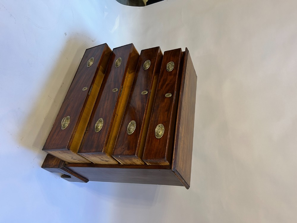 A George III dark mahogany hall chest of drawers with four graduated drawers, oval brass handles, and bracket feet. View IV
