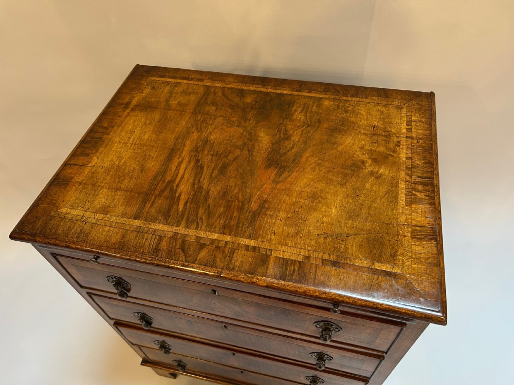 A Georgian Revival walnut bachelors chest featuring four drawers with brass drop handles, a brushing slide, and bracket feet. View II