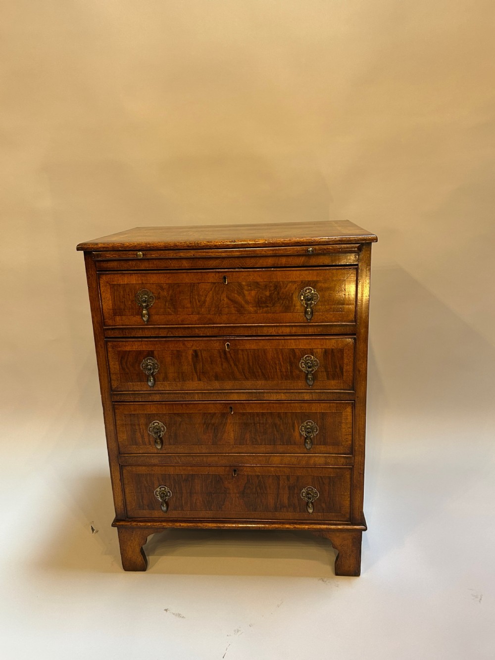 A Georgian Revival walnut bachelors chest featuring four drawers with brass drop handles, a brushing slide, and bracket feet. View V