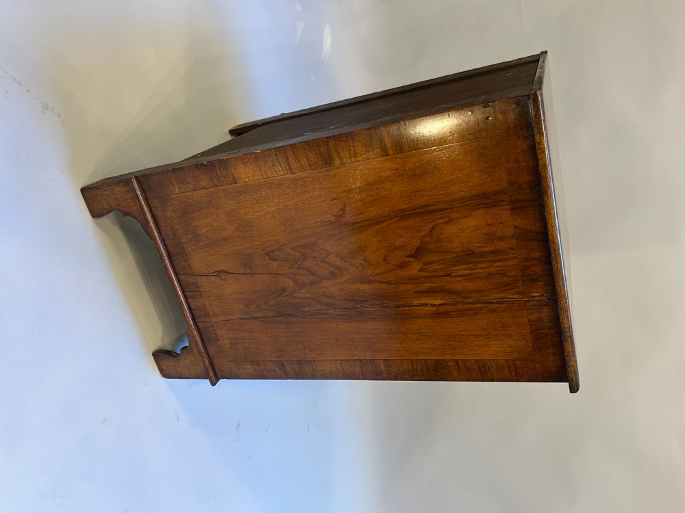 A Georgian Revival walnut bachelors chest featuring four drawers with brass drop handles, a brushing slide, and bracket feet. View X