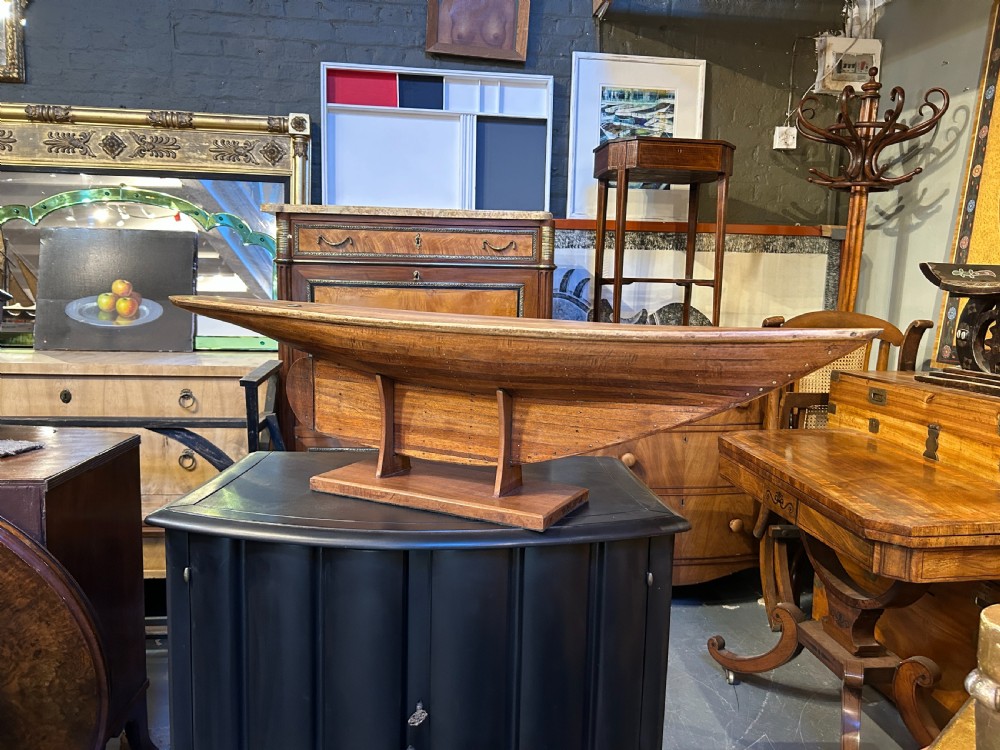 A vintage carved wooden pond yacht hull with a natural timber grain finish resting on a custom display stand. View VI