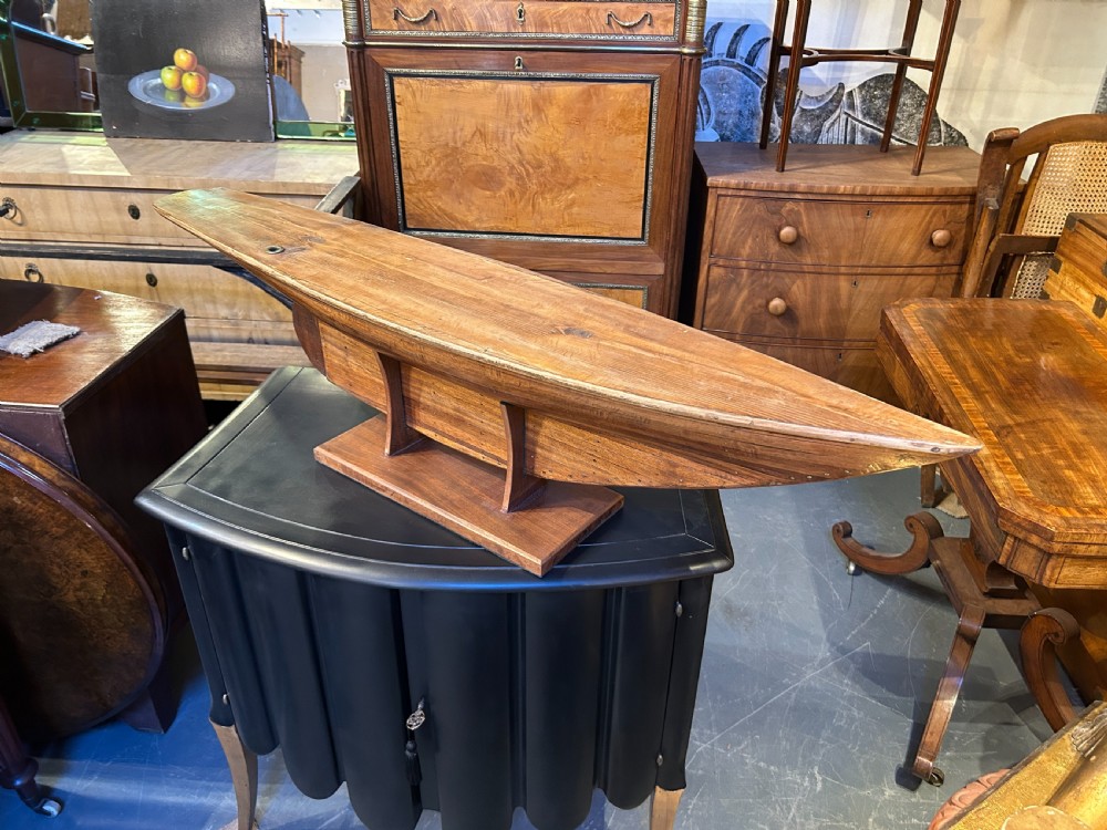 A vintage carved wooden pond yacht hull with a natural timber grain finish resting on a custom display stand. View VII