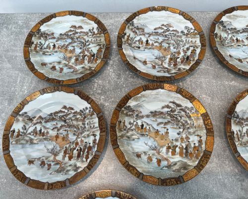 fig 1. A set of twelve circular Japanese Satsuma earthenware plates featuring hand-painted landscape scenes with figures framed by wide gilded decorative borders.