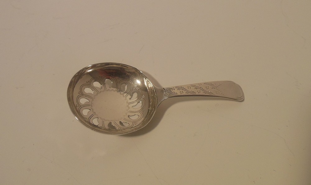 A Georgian sterling silver caddy spoon featuring a rounded pierced bowl and an engraved handle.