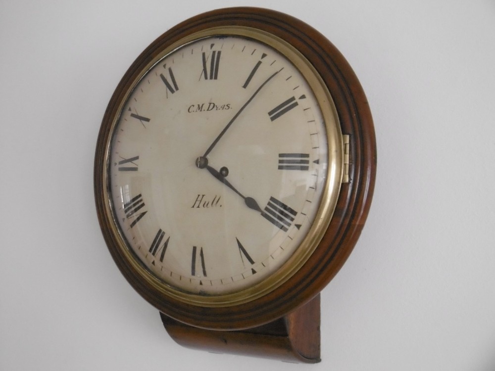 An antique Victorian drop dial wall clock featuring a rounded mahogany wooden frame, a brass-rimmed glass door, and a white dial displaying Roman numerals.
