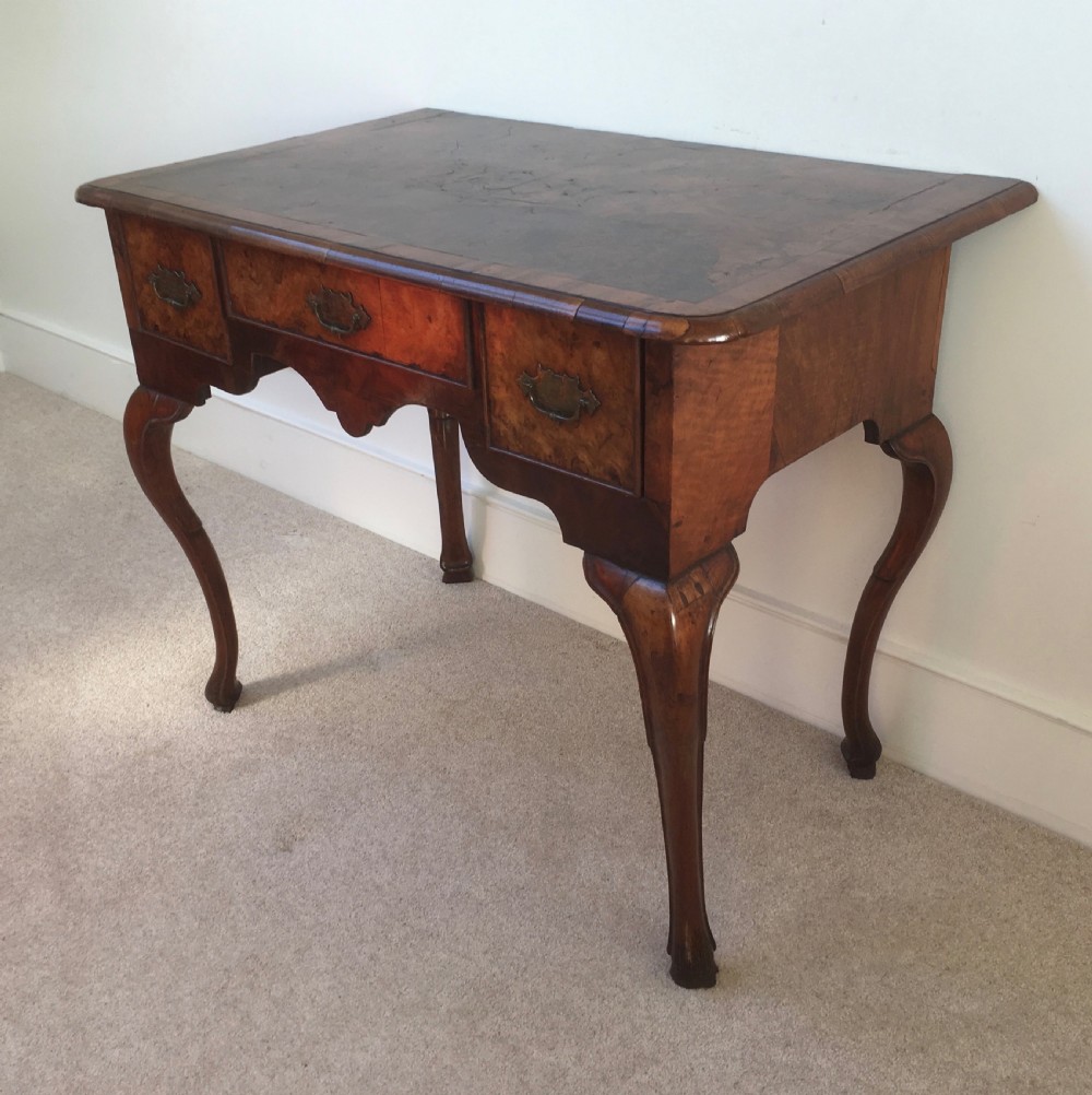 An eighteenth-century George II burr walnut lowboy featuring three drawers, brass handles, a shaped apron, and four slender cabriole legs. View II