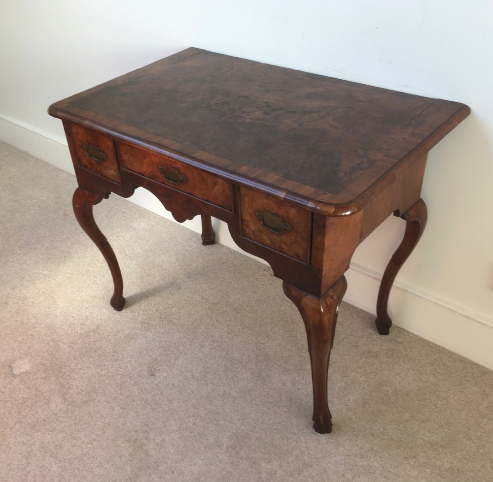 An eighteenth-century George II burr walnut lowboy featuring three drawers, brass handles, a shaped apron, and four slender cabriole legs. View IV
