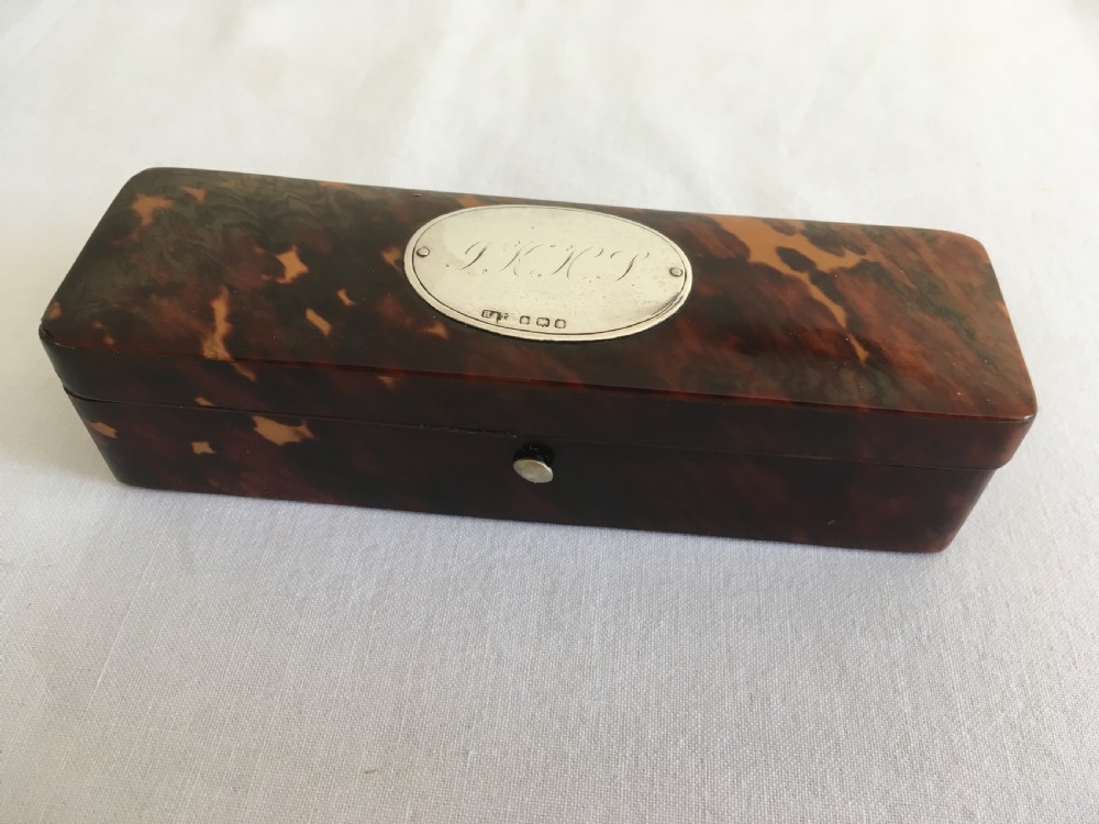 A rectangular mottled tortoiseshell box with rounded corners and an oval silver monogrammed plaque mounted on the lid.