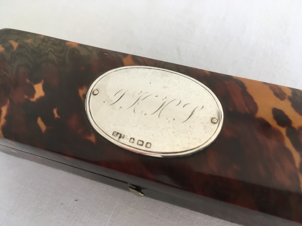 A rectangular mottled tortoiseshell box with rounded corners and an oval silver monogrammed plaque mounted on the lid. View IV