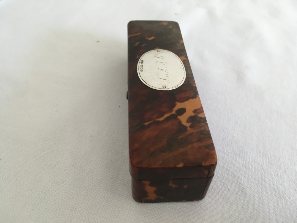 A rectangular mottled tortoiseshell box with rounded corners and an oval silver monogrammed plaque mounted on the lid. View V