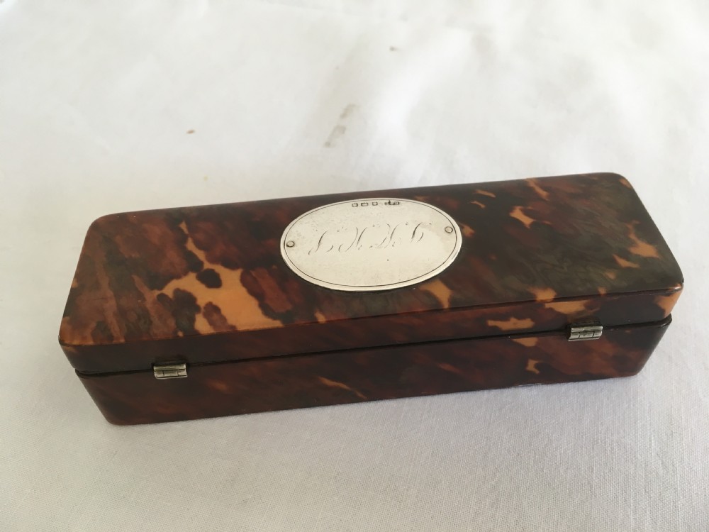 A rectangular mottled tortoiseshell box with rounded corners and an oval silver monogrammed plaque mounted on the lid. View VI