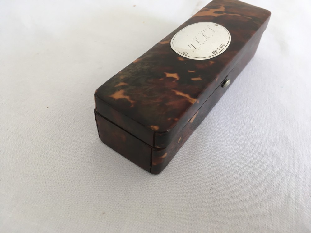 A rectangular mottled tortoiseshell box with rounded corners and an oval silver monogrammed plaque mounted on the lid. View VII