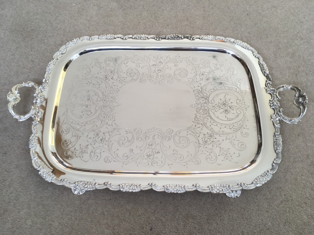 A 19th-century rectangular silver-plated serving tray featuring engraved foliate scrollwork, a decorative rim, and two cast side handles.