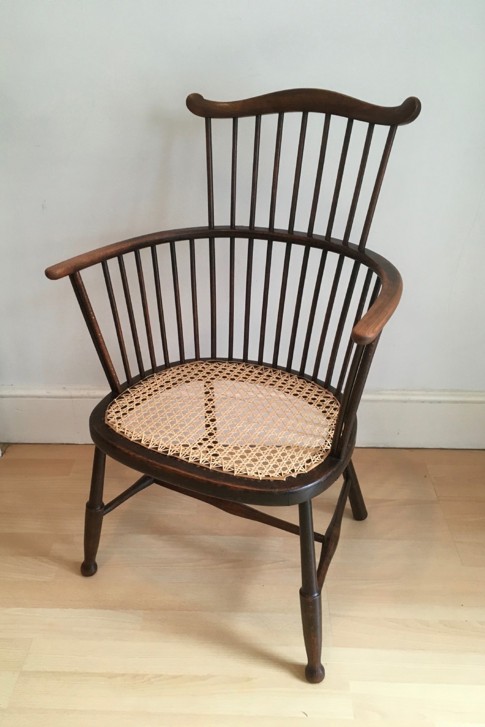 A dark stained wooden stick-back armchair featuring a comb crest rail, spindle uprights, curved armrests, and a woven natural cane seat.