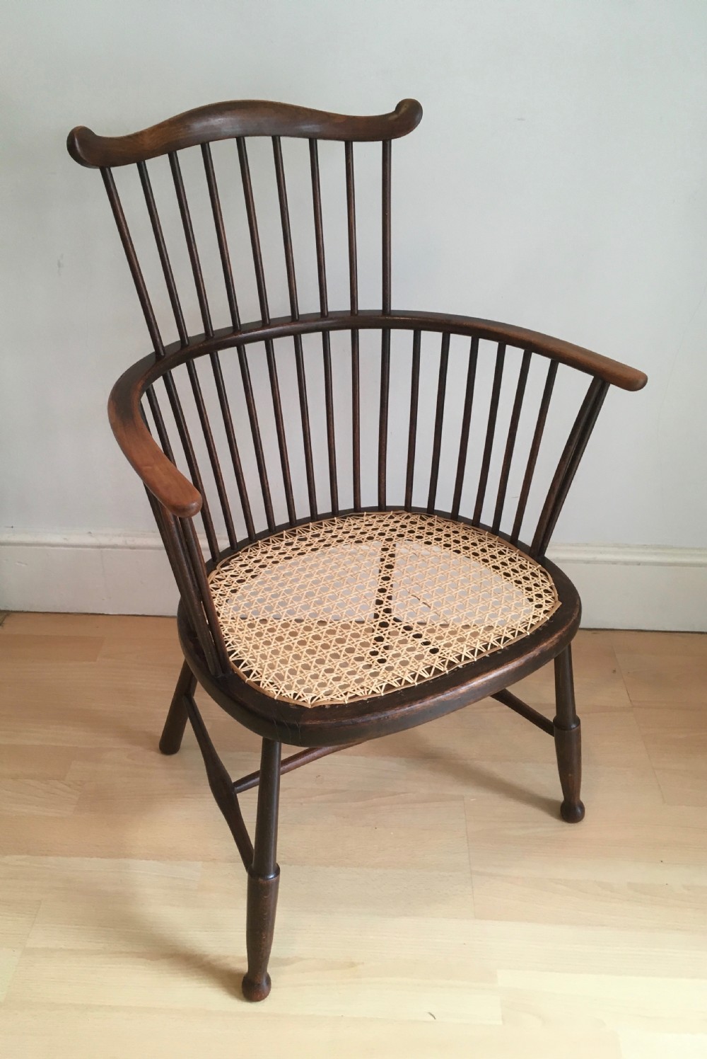 A dark stained wooden stick-back armchair featuring a comb crest rail, spindle uprights, curved armrests, and a woven natural cane seat. View II