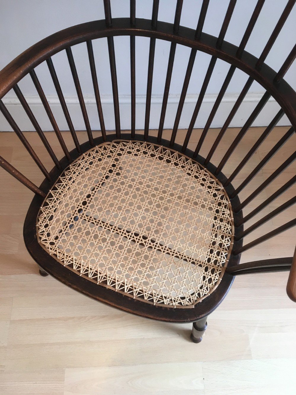 A dark stained wooden stick-back armchair featuring a comb crest rail, spindle uprights, curved armrests, and a woven natural cane seat. View III