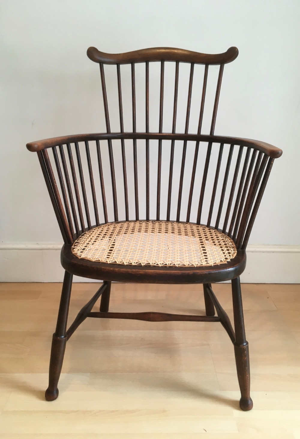 A dark stained wooden stick-back armchair featuring a comb crest rail, spindle uprights, curved armrests, and a woven natural cane seat. View VI