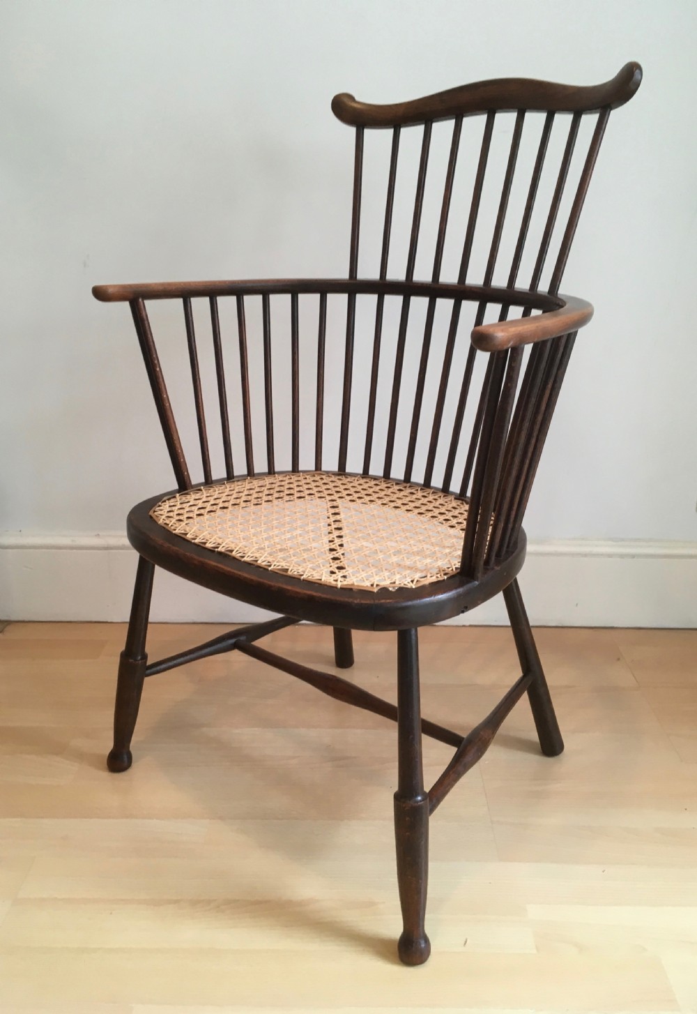 A dark stained wooden stick-back armchair featuring a comb crest rail, spindle uprights, curved armrests, and a woven natural cane seat. View VII