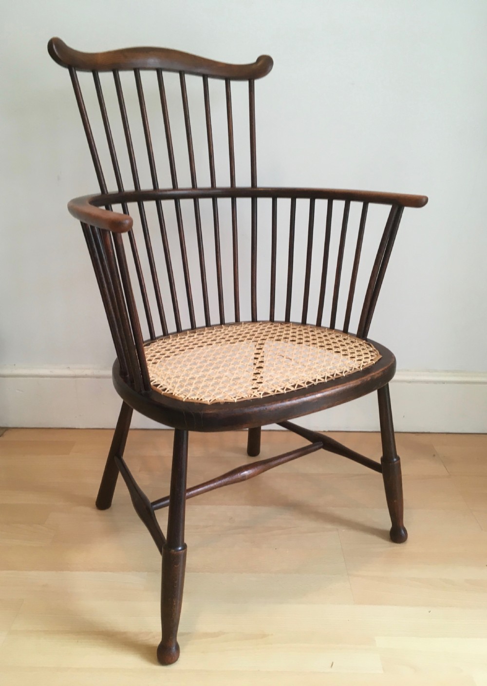 A dark stained wooden stick-back armchair featuring a comb crest rail, spindle uprights, curved armrests, and a woven natural cane seat. View VIII