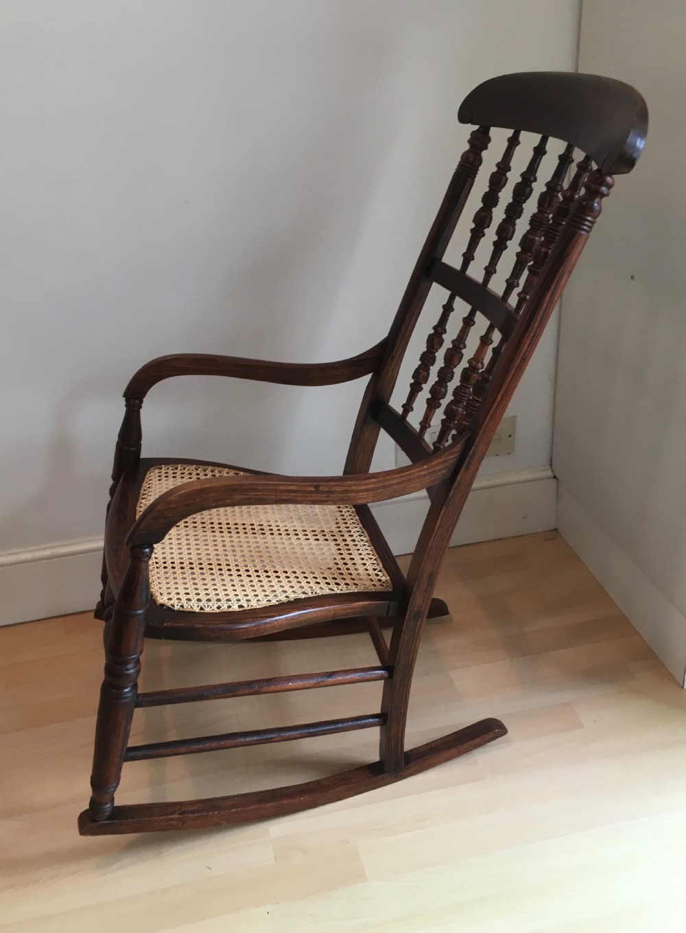 A dark wood 19th-century spindle back rocking chair featuring a woven cane seat, turned spindles, and curved armrests resting on curved runners. View III