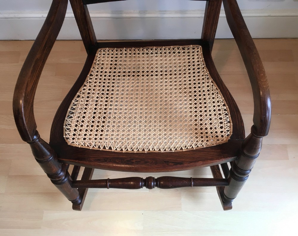 A dark wood 19th-century spindle back rocking chair featuring a woven cane seat, turned spindles, and curved armrests resting on curved runners. View IV
