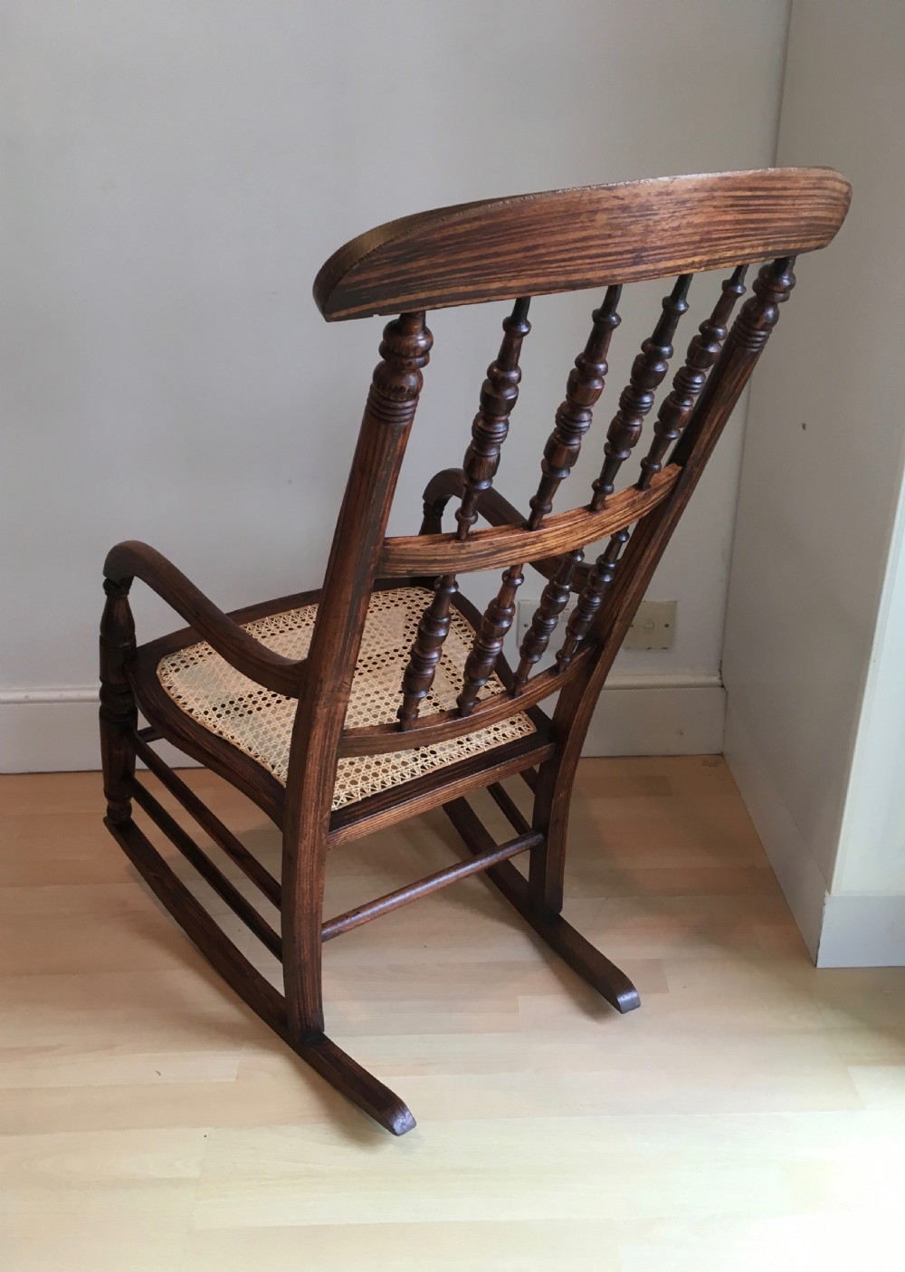 A dark wood 19th-century spindle back rocking chair featuring a woven cane seat, turned spindles, and curved armrests resting on curved runners. View V