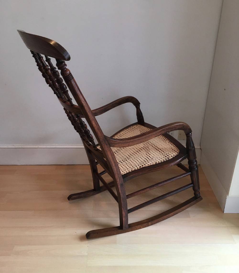 A dark wood 19th-century spindle back rocking chair featuring a woven cane seat, turned spindles, and curved armrests resting on curved runners. View VII