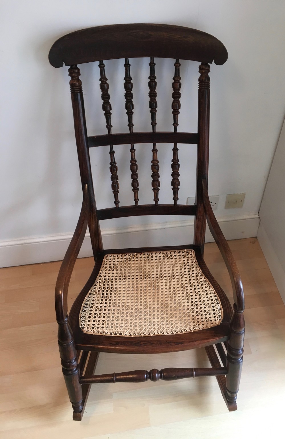 A dark wood 19th-century spindle back rocking chair featuring a woven cane seat, turned spindles, and curved armrests resting on curved runners. View IX