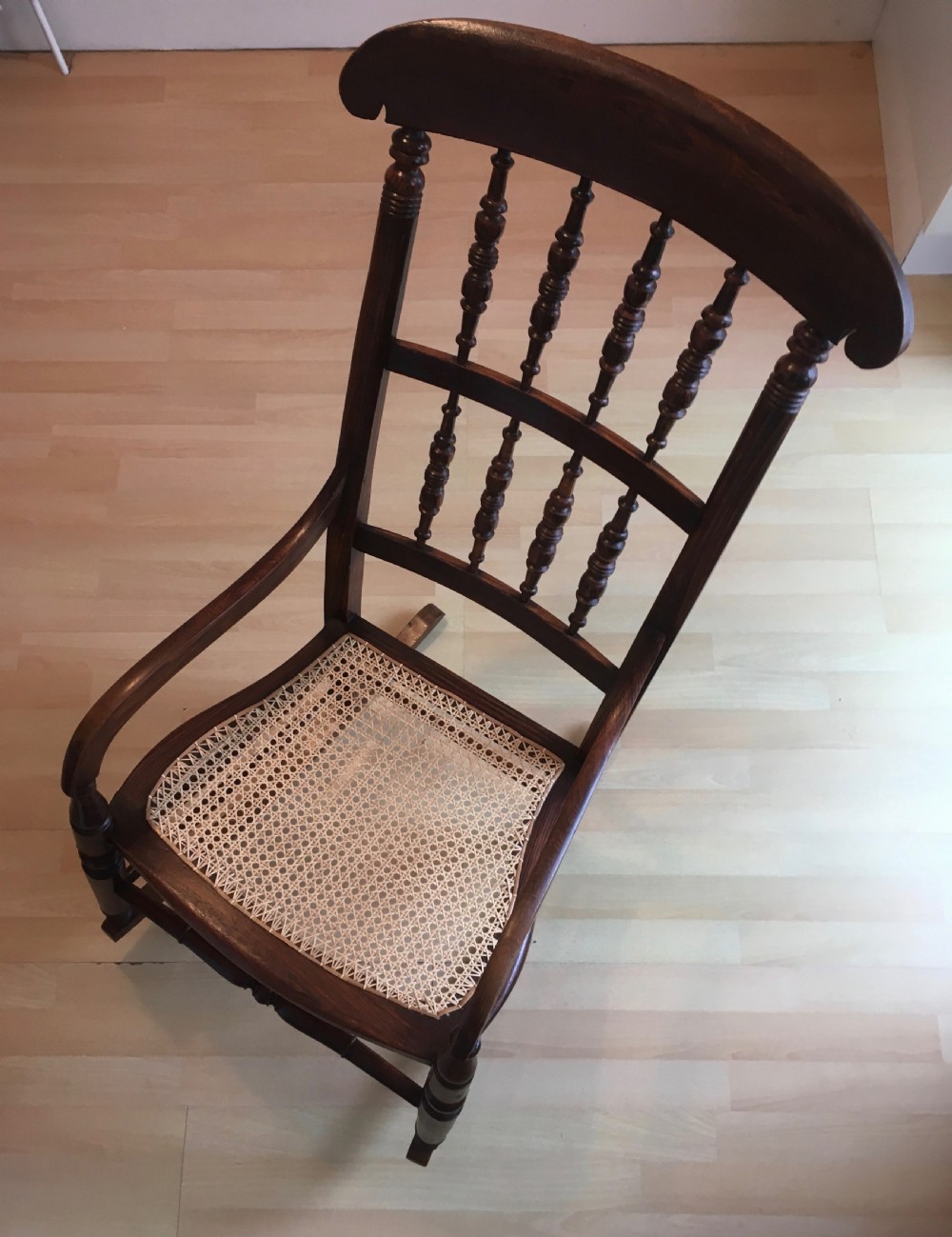 A dark wood 19th-century spindle back rocking chair featuring a woven cane seat, turned spindles, and curved armrests resting on curved runners. View X