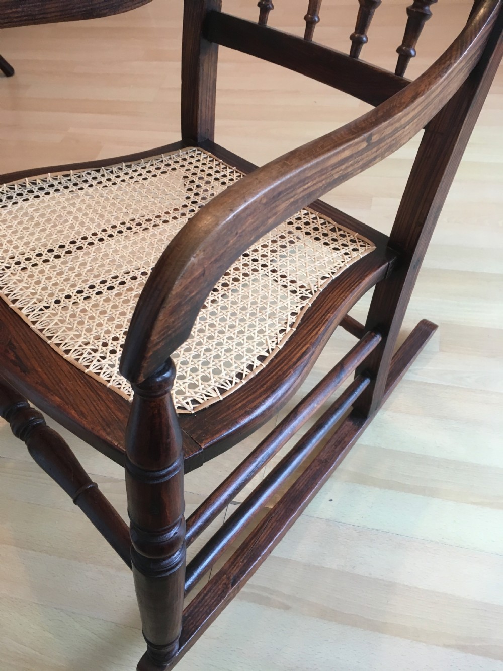 A dark wood 19th-century spindle back rocking chair featuring a woven cane seat, turned spindles, and curved armrests resting on curved runners. View XI