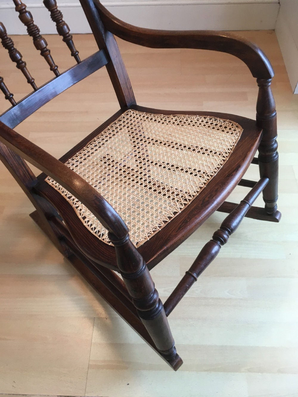 A dark wood 19th-century spindle back rocking chair featuring a woven cane seat, turned spindles, and curved armrests resting on curved runners. View XII