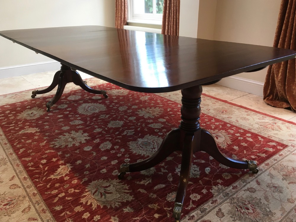 A 19th-century mahogany extendable dining table featuring a polished rectangular top with rounded corners, supported by two turned pillar pedestals on splayed legs with brass castors.