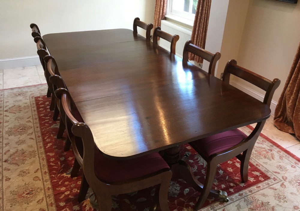 A 19th-century mahogany extendable dining table featuring a polished rectangular top with rounded corners, supported by two turned pillar pedestals on splayed legs with brass castors. View II