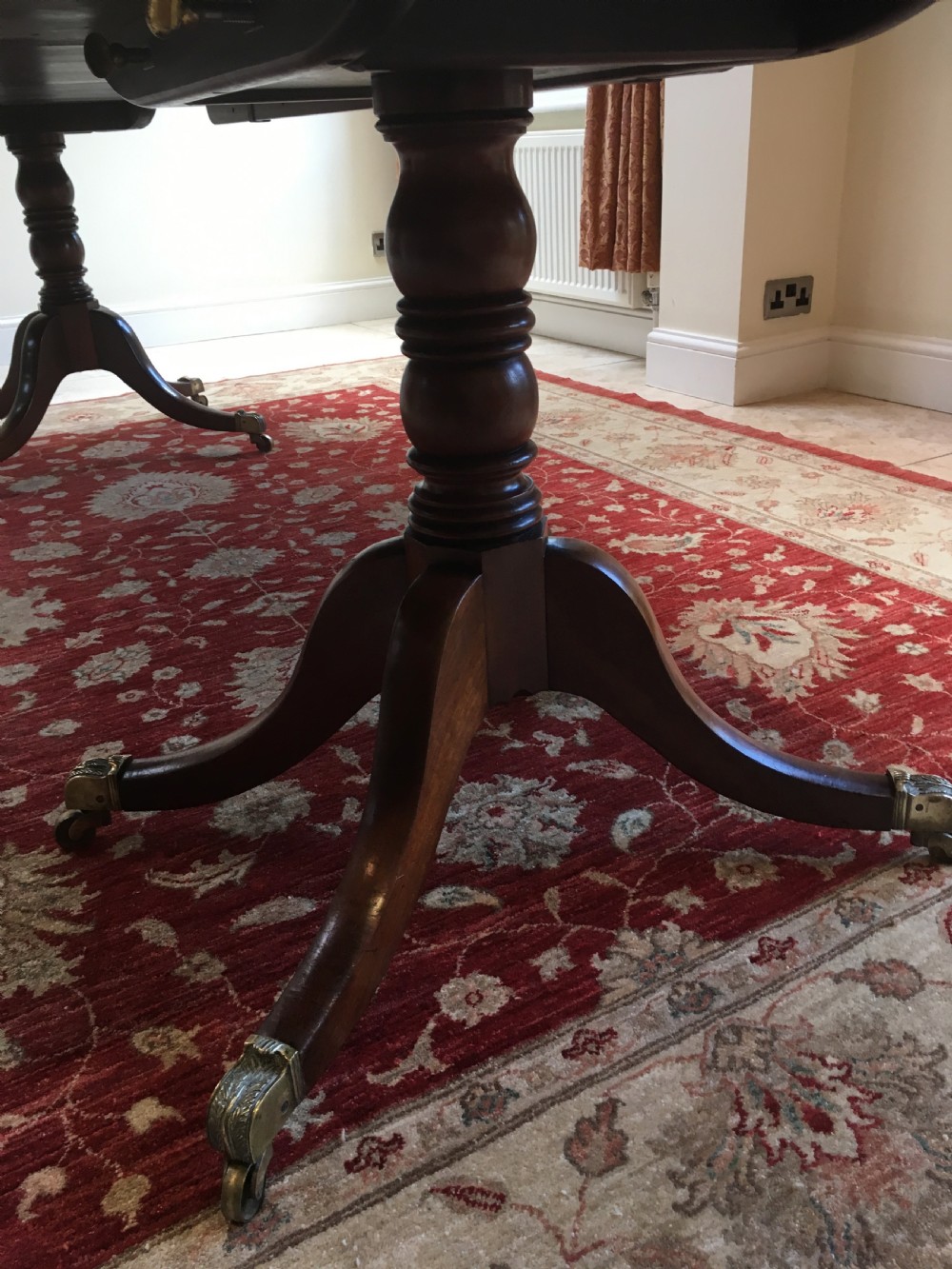 A 19th-century mahogany extendable dining table featuring a polished rectangular top with rounded corners, supported by two turned pillar pedestals on splayed legs with brass castors. View IV