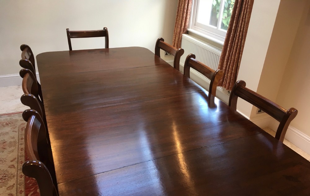 A 19th-century mahogany extendable dining table featuring a polished rectangular top with rounded corners, supported by two turned pillar pedestals on splayed legs with brass castors. View VI